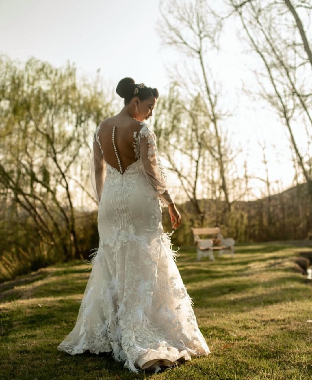 salome Lace Mermaid Gown with Sheer Bateau Neckline and Feather Detail The Salome gown is a captivating fusion of bold glamour and soft romance. Designed for the bride who desires sophistication with a hint of drama, this lace mermaid silhouette features delicate layering, intricate detailing, and graceful textures that move with you. ✨ Design Highlights: ✔ Sweetheart Bodice with Bateau Illusion Neckline – A flattering sweetheart bustline beneath sheer nude tulle creates a refined and modern décolletage. ✔ Lace Bodice & Illusion Back – Detailed lace appliqués flow seamlessly into a sheer illusion back, finished with a row of elegant bridal buttons. ✔ Fitted Mermaid Skirt – Figure-hugging through the hips and flaring out with soft feather and lace detailing for a touch of couture drama. ✔ Bishop Lace Sleeves – Romantic, voluminous sleeves crafted in lace, gathered into wide soft tulle cuffs for a regal finish. ✔ Elegant Button Closure – Classic bridal buttons cascade down the sheer back for timeless charm. 💫 Customization Options: ✅ Custom sizing for a flawless fit ✅ Option to remove or adjust sleeve length ✅ Available with or without feather detailing on the skirt ✅ Lace available in soft white, ivory, or nude underlayers 🕊 Salome is made for the bride who isn’t afraid to be unforgettable—refined, bold, and brimming with texture. 🕊 📞 Schedule your private consultation today! 📧 info@bestersbridal.co.za | 📱 084 268 1354 Sweetheart Bodice • Illusion Neckline & Back • Mermaid Silhouette • Feather & Lace Skirt • Bishop Sleeves with Tulle Cuffs