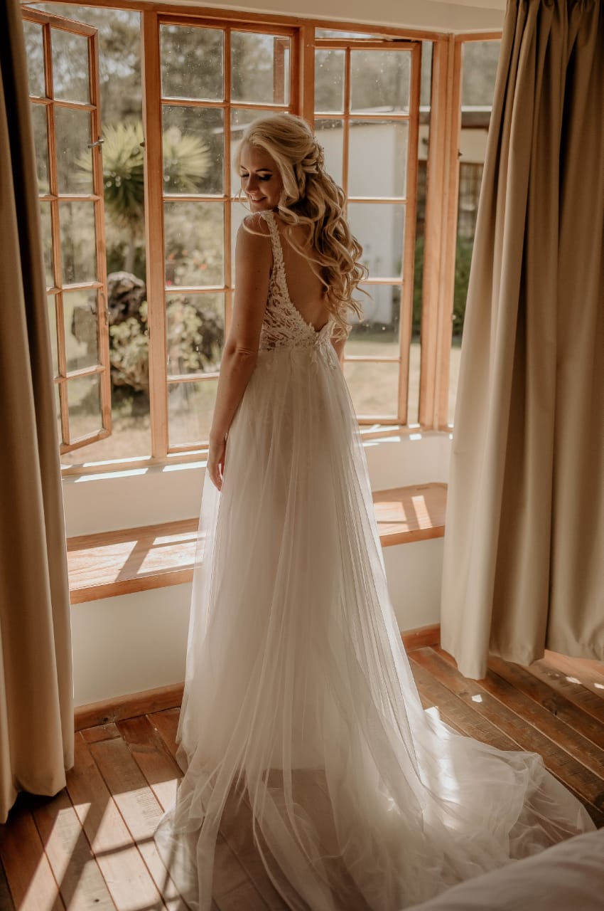 DRESS ELOISE A romantic bridal gown featuring a sheer V-neckline bodice, intricately embroidered with beaded lace for a touch of sparkle and sophistication. The design flows into layers of soft tulle that form a graceful A-line skirt, creating an airy and ethereal silhouette. With a low open back and a delicate short train, this gown perfectly balances elegance and comfort. The button closure adds a timeless finishing detail to this effortlessly chic bridal look. The dress is available for custom orders, tailored to your exact measurements in the colour of your choice. You can personalize it further by selecting either a long or short train, with short or long sleeves, and with or without a slit.